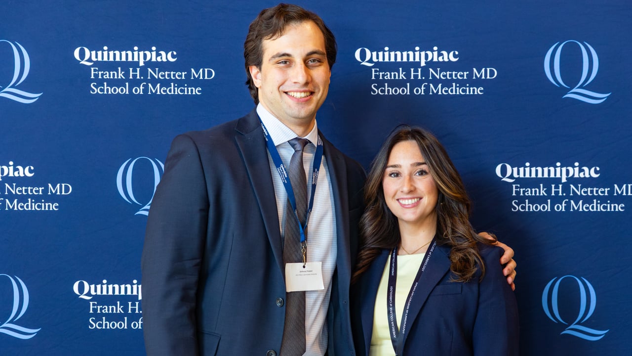 Two students pose in front of a Quinnipiac backdrop.