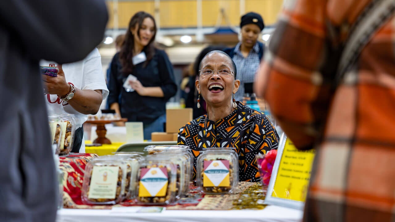 A vendor smiles while selling a food product at their table.