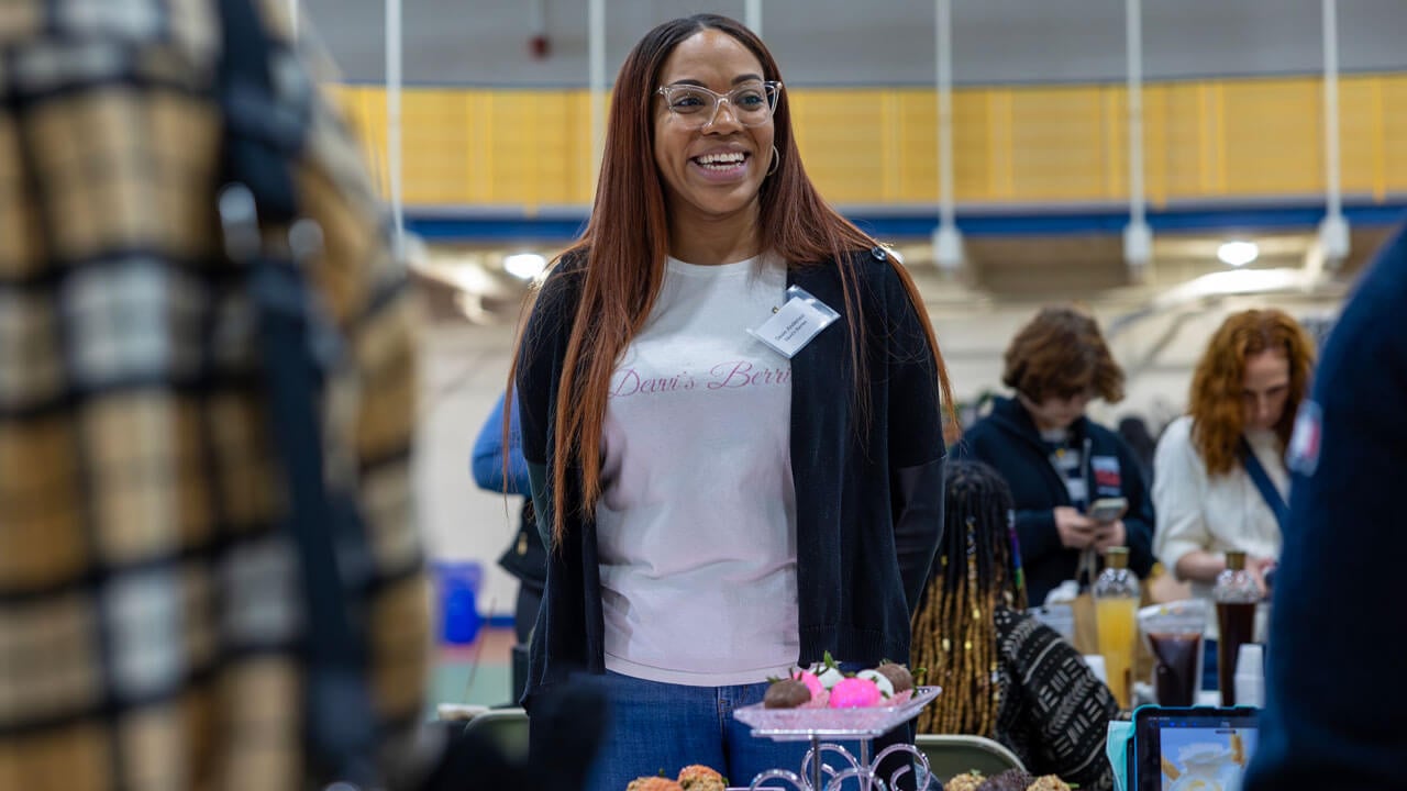 A vendor at Devvi's Berries smiles in front of their table.