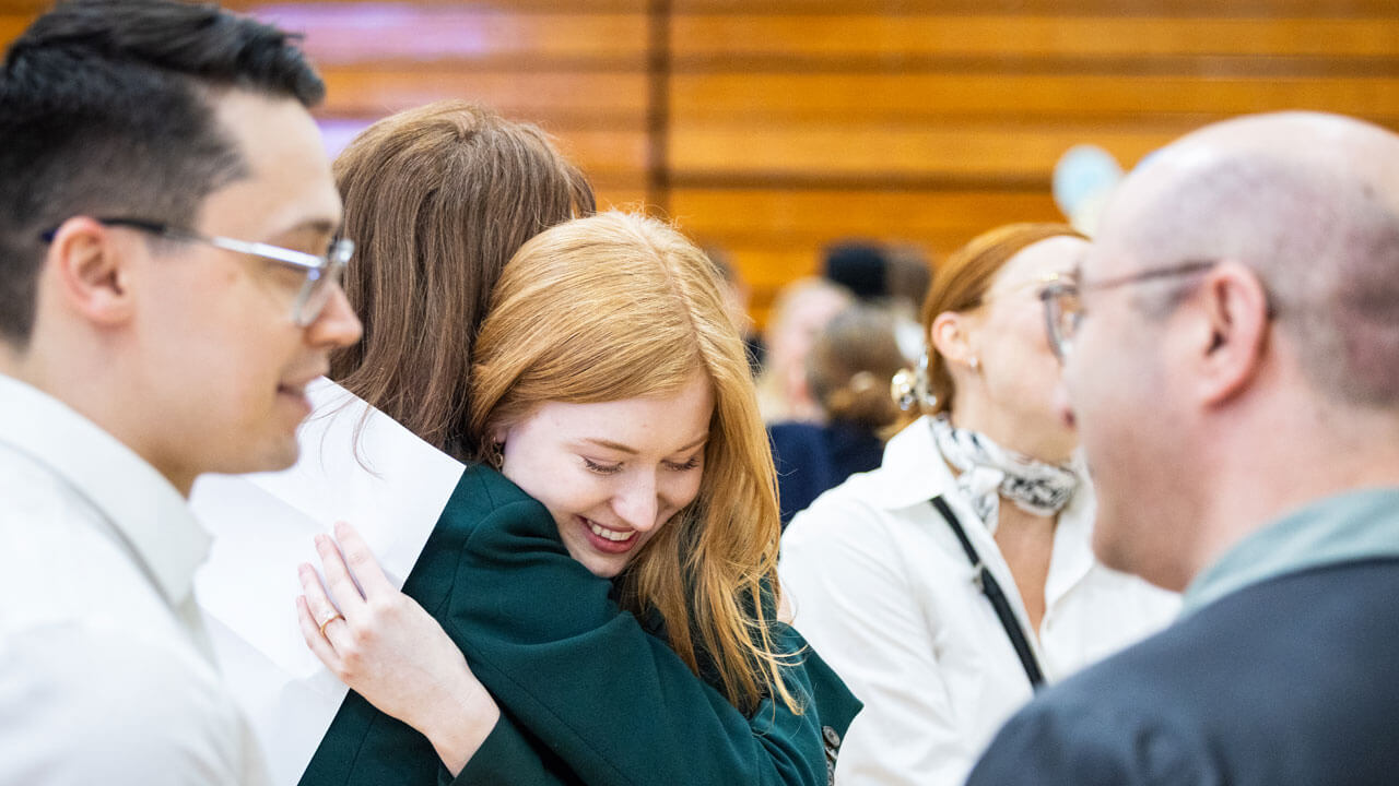 Student hugs a loved one while looking down at her placement envelope