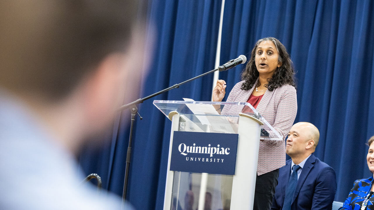 School of Medicine administrator speaks at a podium to students and their loved ones