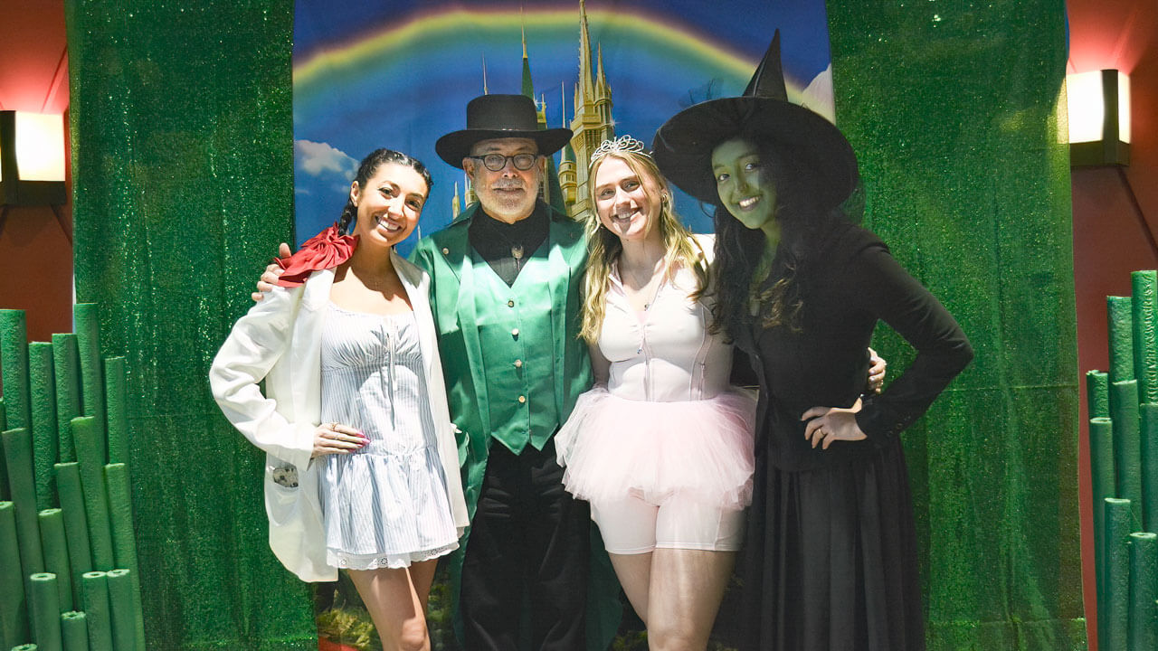 Participants pose for a photo in their costumes in front of a rainbow backdrop.