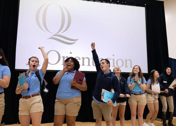 A group of orientation leaders standing on stage with arms in the air to welcome new students during Orientation