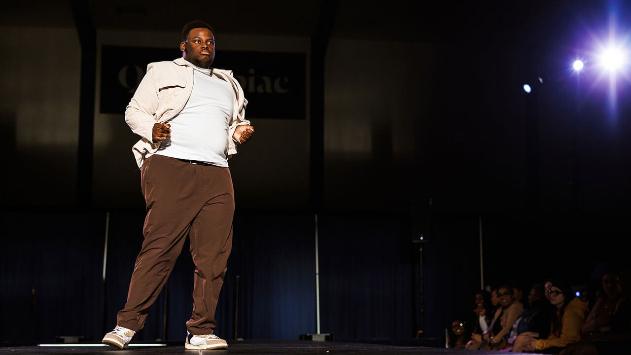 black man wearing a white shirt and jacket with brown pants dances on stage