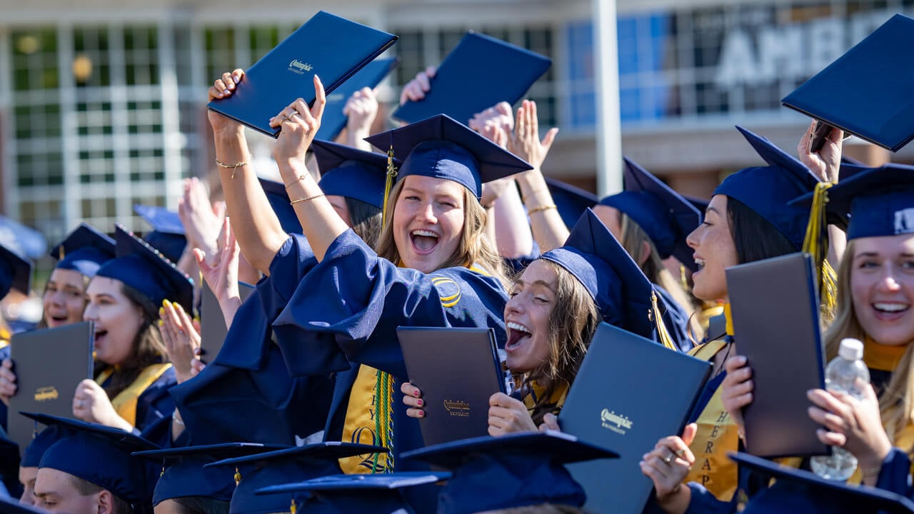 Grads in the crowd hold up their diplomas in excitement