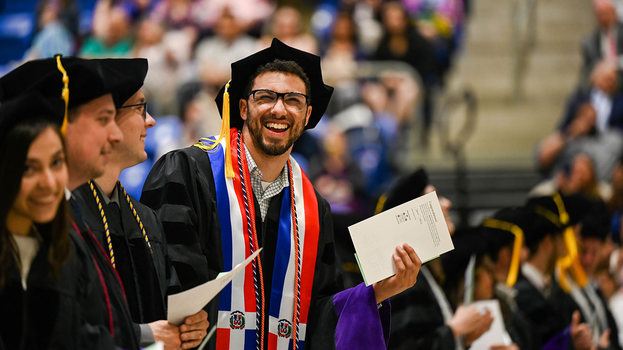 A graduate leans out of his seat to smile at the camera