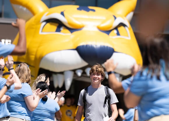 A student smiles as he walks beneath an inflated Bobcat and Orientation Leaders clap