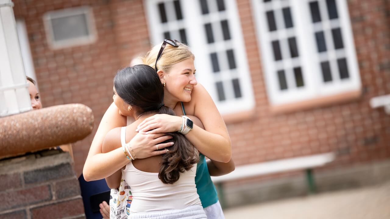 Two students hug with smiles on their faces