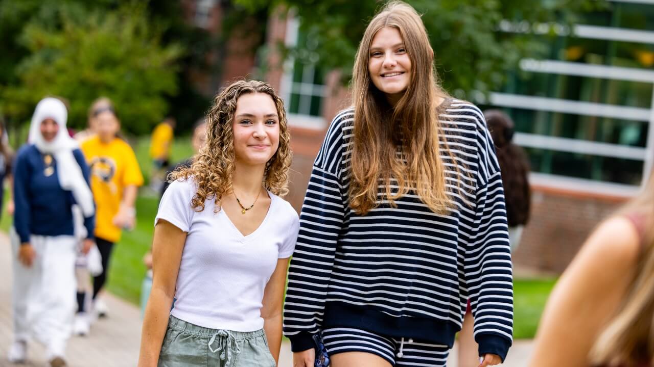 Two new students smile together while walking