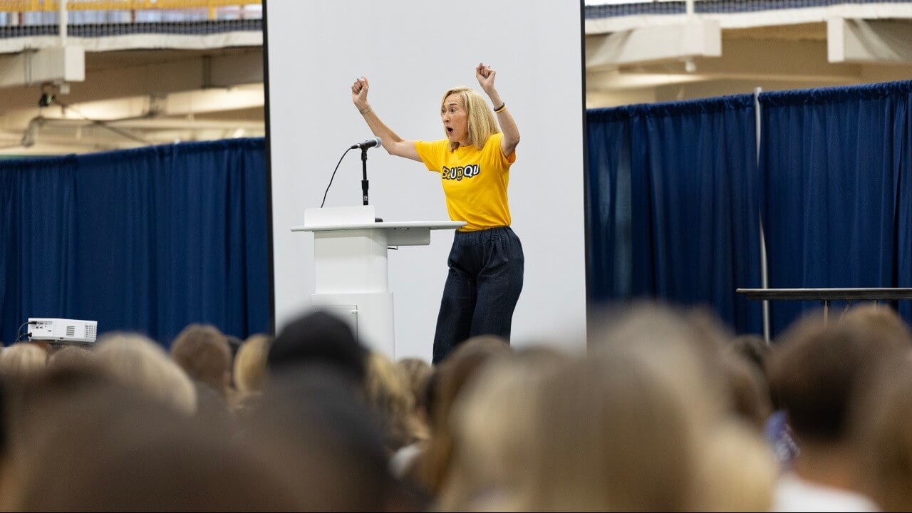 Marie Hardin celebrates the class of 2030 with her hands in the air at podium