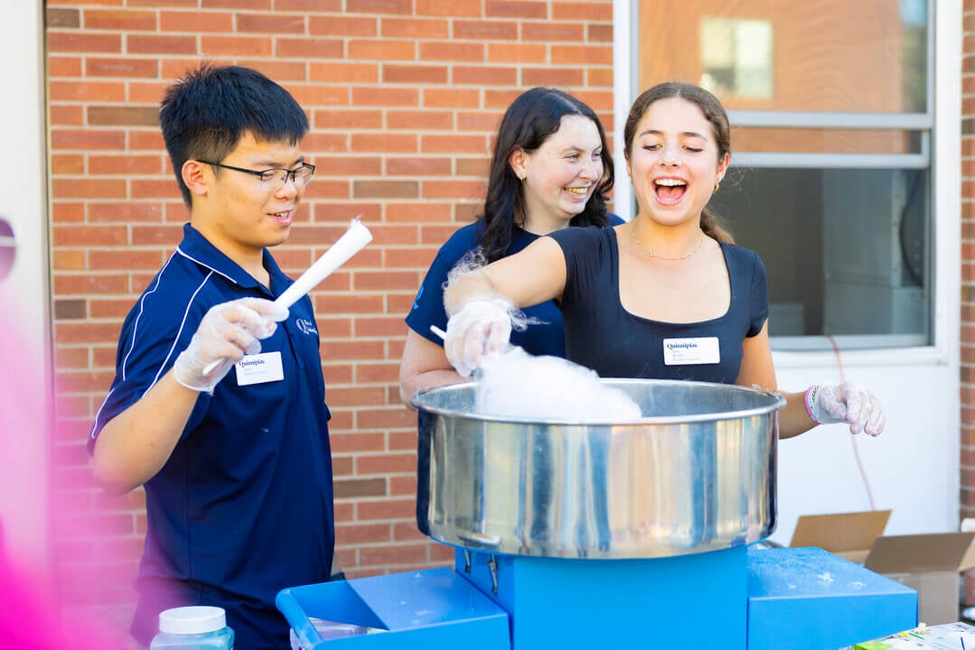 Three Quinnipiac Residential Assistants cheerfully make cotton candy for residents for their first night back.