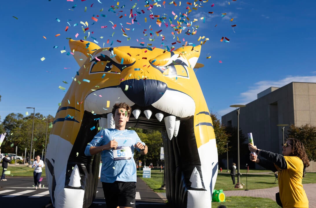 A Quinnipiac student finished the Roaring Start 5K and runs through the inflatable bobcat's mouth with confetti flying in the air.