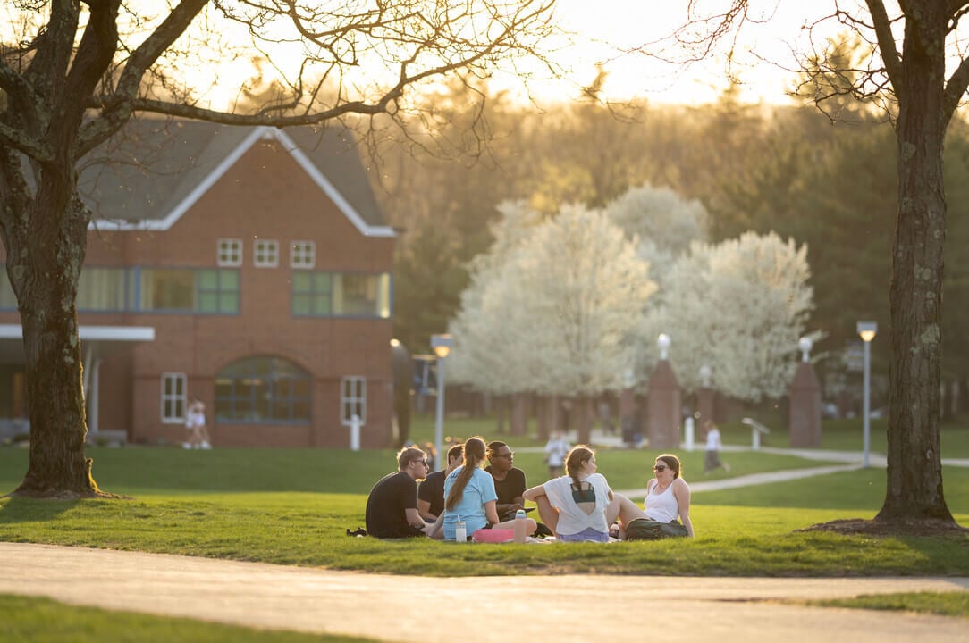 Quinnipiac students sit on a blanket on the Quad on during a springtime sunset in front of the Echlin building.