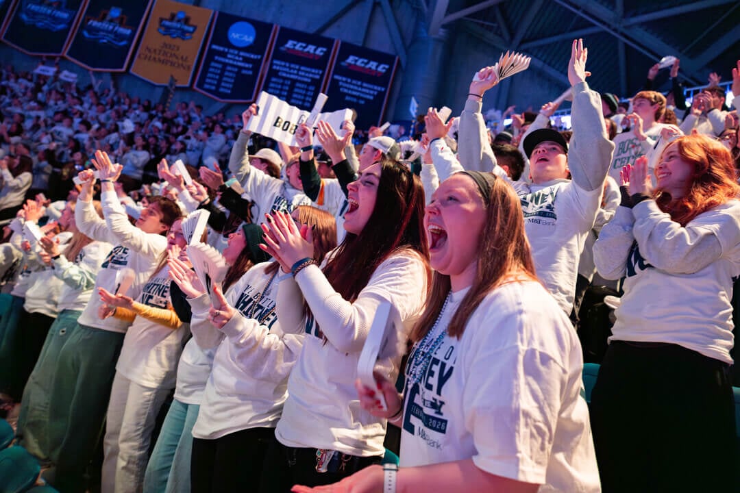 A crowd of Quinnipiac students wearing Quinnipiac merch cheer on their hockey team.