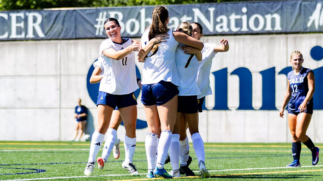 Four soccer players embrace on the field.