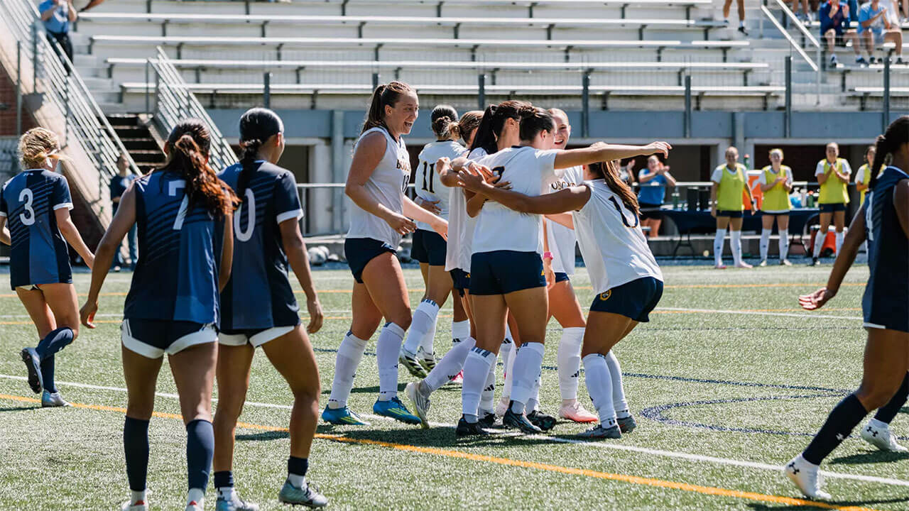 Soccer players smile and embrace on the field.