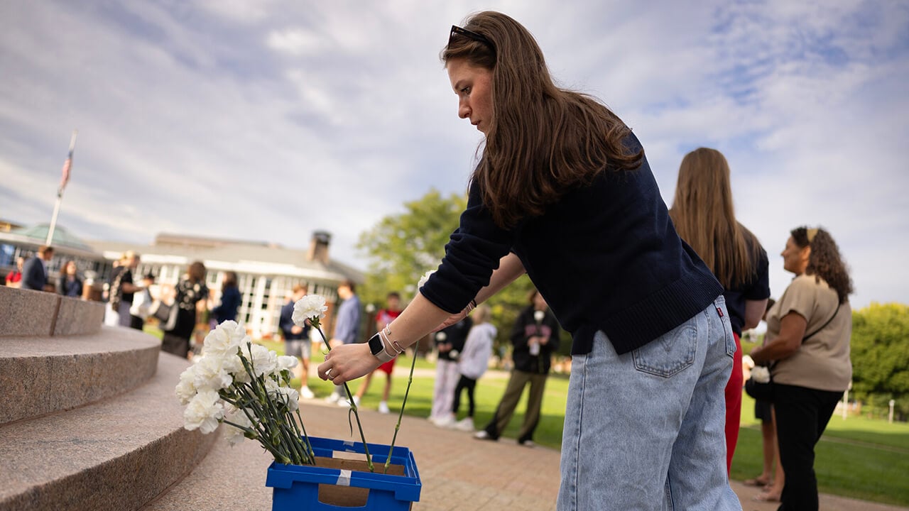 Student picking up carnation from flower bucket.