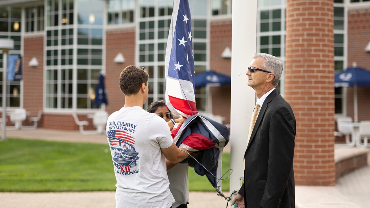 Two students helping Jason Burke raise the flag to half mast
