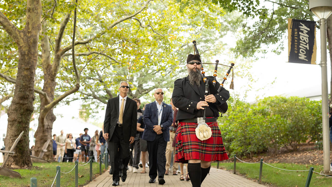 Bagpiper leading procession down Bobcat Way