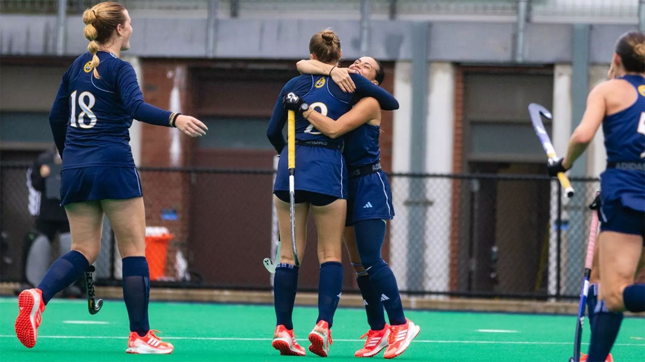 Two field hockey players embrace on the field.
