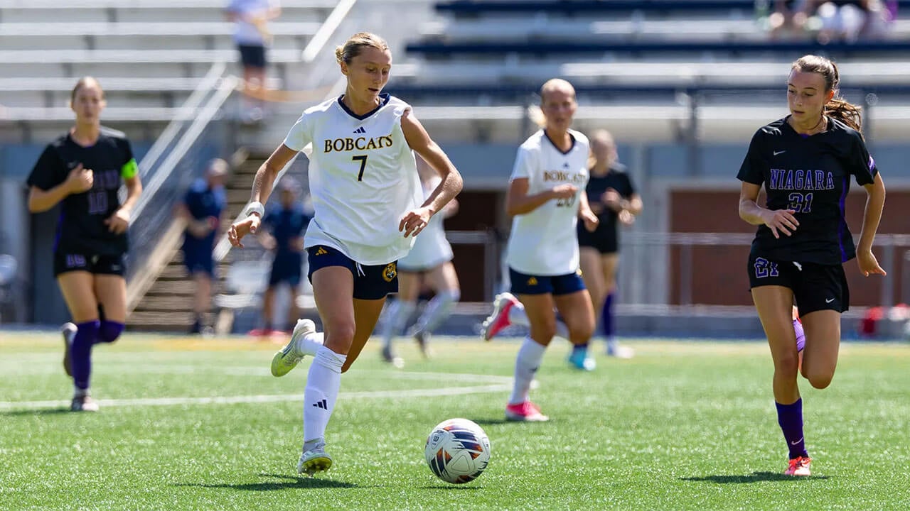 Soccer players chase after the ball.