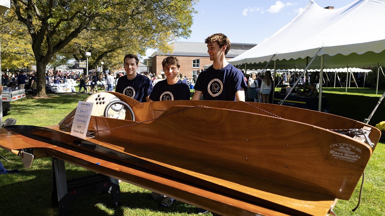 Three students standing in front of boat.