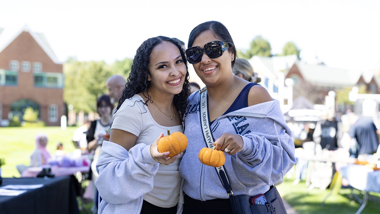 Two people holding small pumpkins.