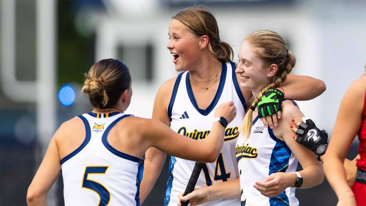 Three members of the women's field hockey team embrace on the field in celebration.