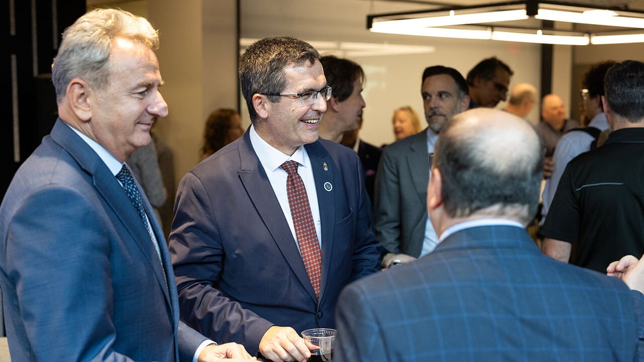Three men in suits stand together in conversation.