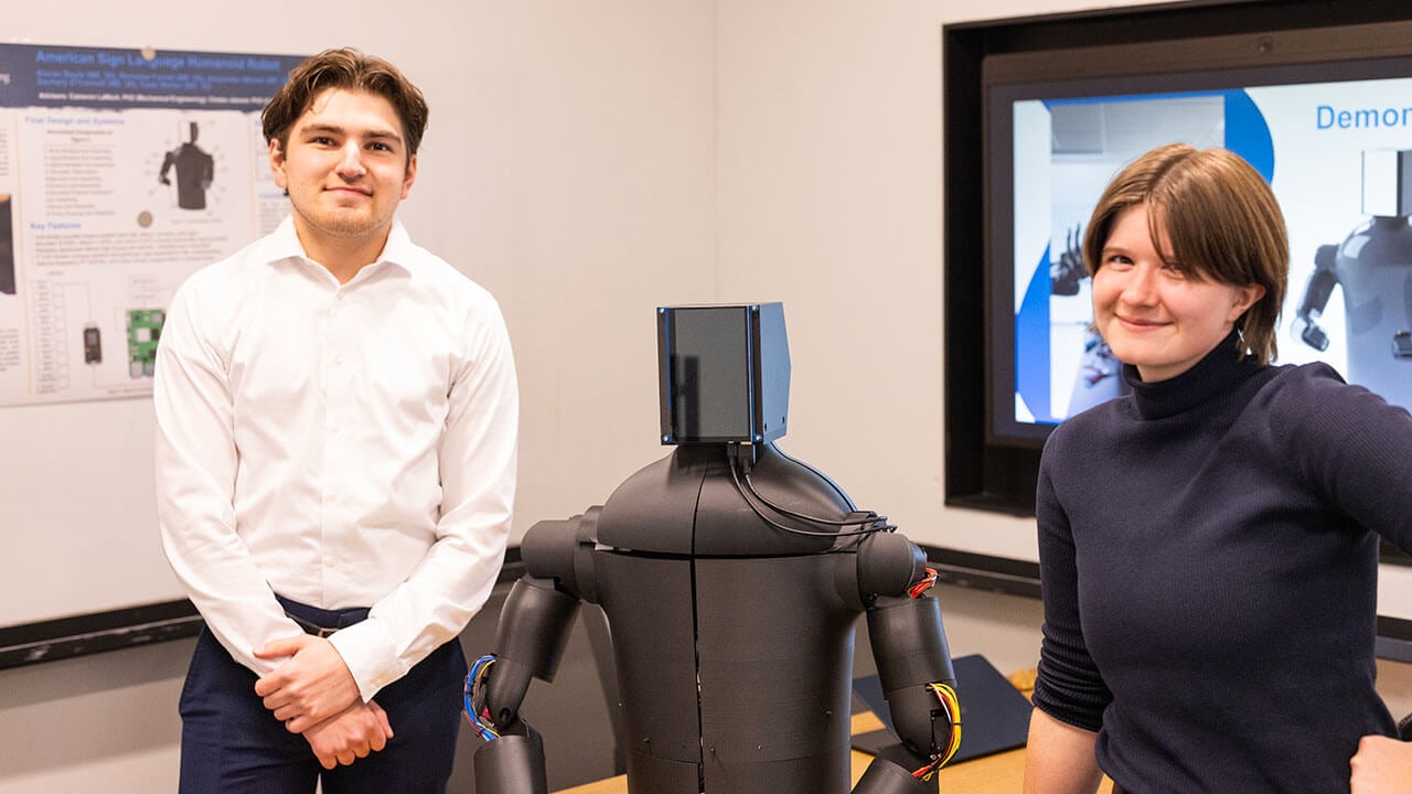 Two students stand with clasroom robot.