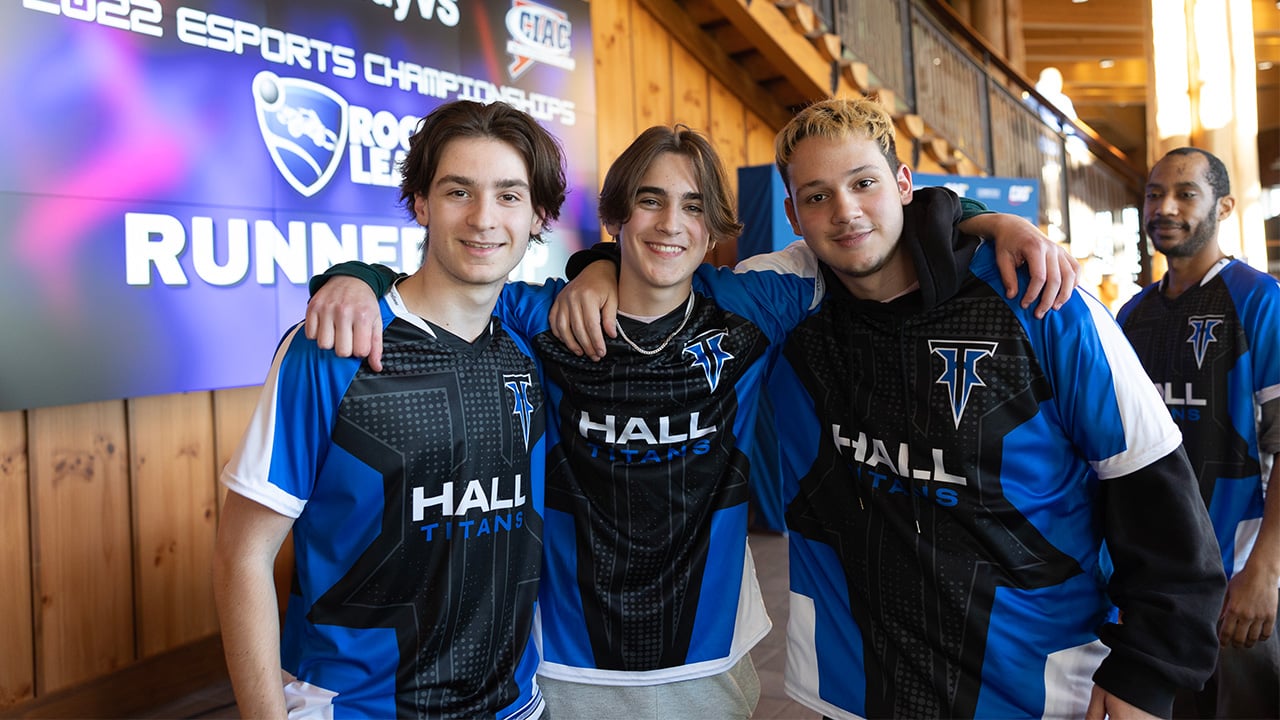 A group of four eSports athletes stands and smiles for a photo wearing shirts that read